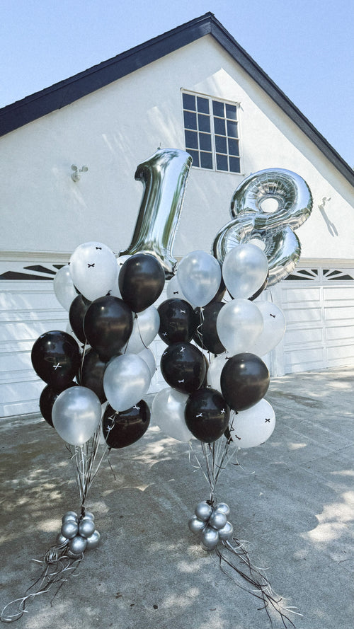 Black and white helium birthday balloon bouquets with oversized silver number balloons positioned above the arrangements.