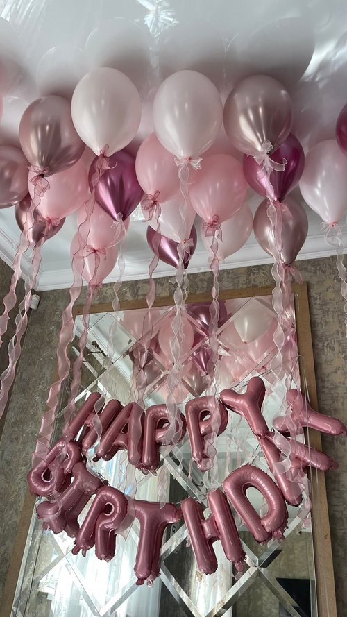 Blush pink, pearl white, and rose gold helium balloons floating across the ceiling with cascading ribbons and metallic Happy Birthday letter balloons.