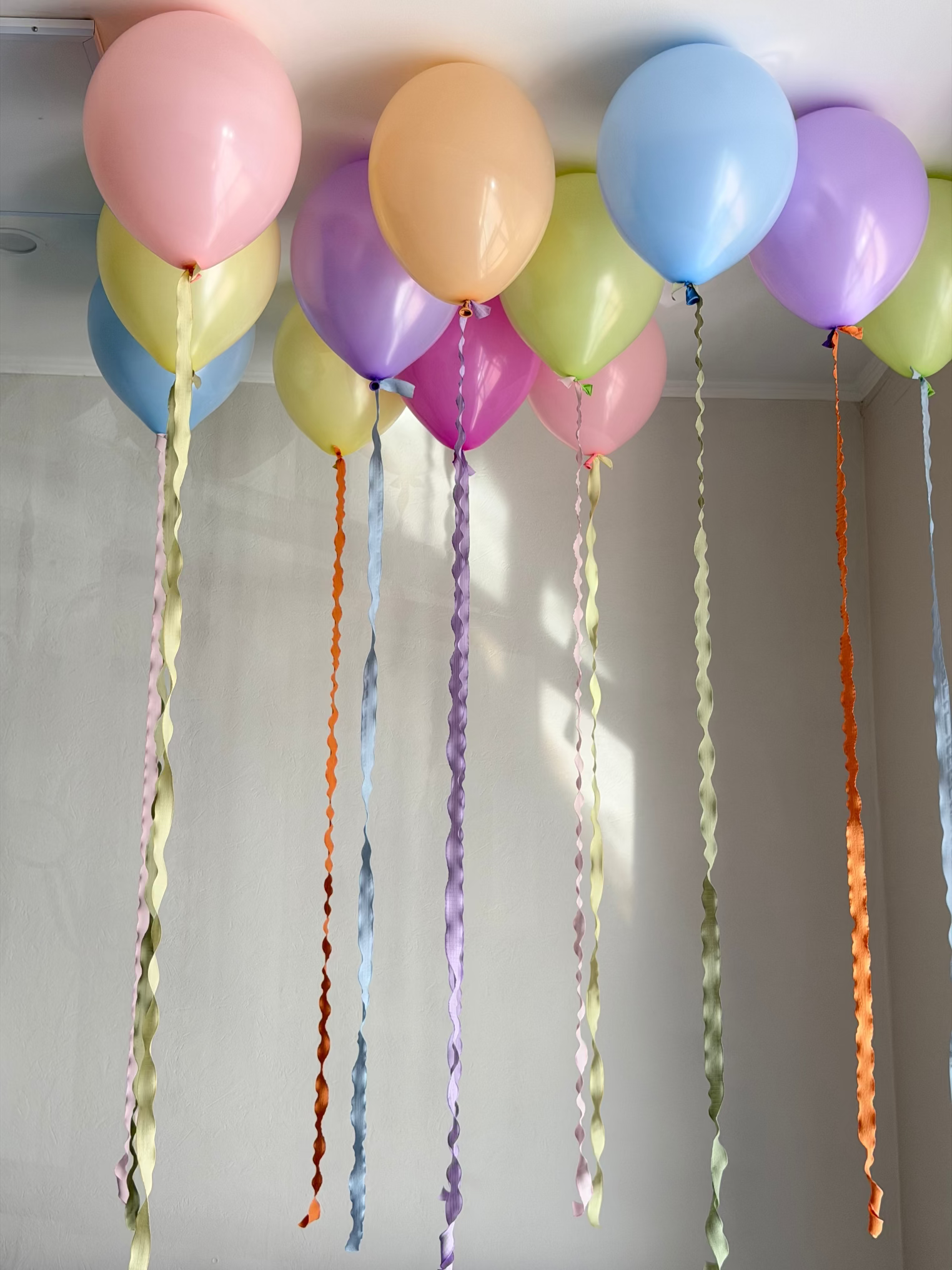 Colorful pastel helium balloons in pink, lavender, baby blue, peach, yellow, and green featuring long custom wavy decorative ribbons. Unique floating balloon decoration by Best Balloons LA, offering luxury balloon delivery in Beverly Hills, Bel Air, and Los Angeles.