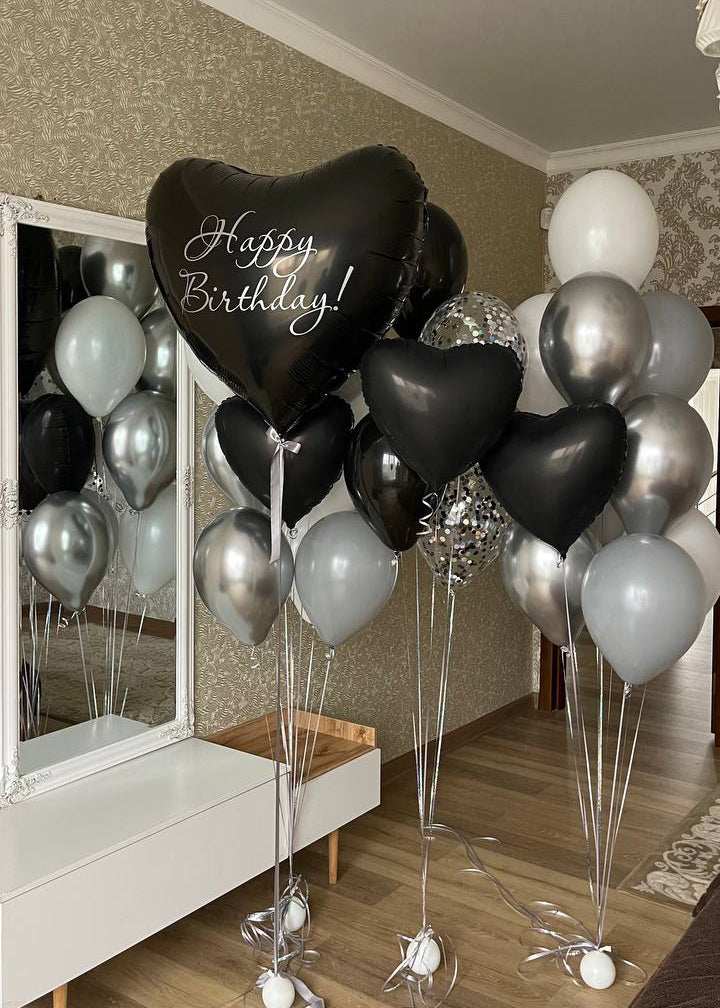Elegant black and silver helium birthday balloon arrangement featuring an oversized black heart-shaped Happy Birthday foil balloon, smaller black heart balloons, metallic silver chrome balloons, white latex balloons, and transparent silver confetti balloons. Luxury monochrome birthday balloon bouquet by Best Balloons LA serving Beverly Hills, Bel Air, Brentwood, and Los Angeles.
