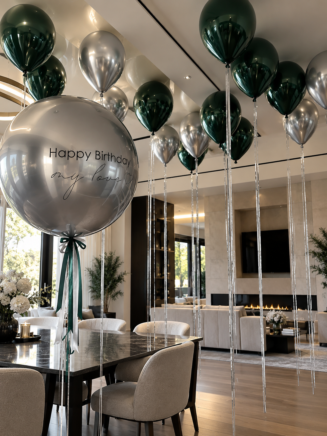 Luxury emerald green and metallic silver helium ceiling balloons decorating a modern living room, featuring a large personalized silver bubble balloon with Happy Birthday My Love lettering and long silver ribbons. Elegant birthday room decoration by Best Balloons LA in Beverly Hills, Bel Air, Brentwood, and Los Angeles.
