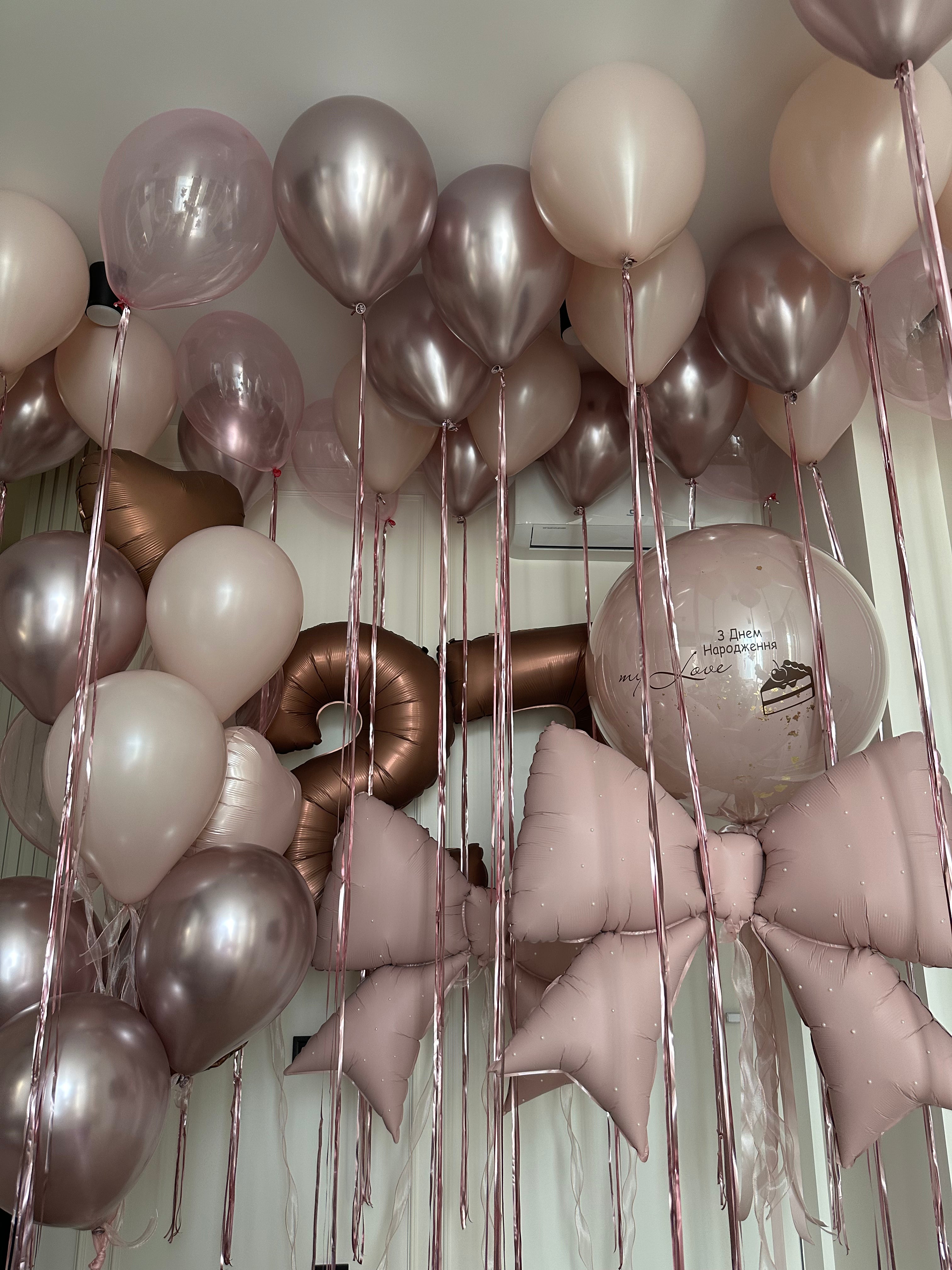 Luxury birthday room balloon decoration featuring floating blush pink, champagne, ivory, and metallic rose gold helium balloons, long rose gold ribbons, oversized pink bow balloons, birthday number balloons, and a personalized clear bubble balloon. Elegant hotel room and home birthday balloon styling by Best Balloons LA.